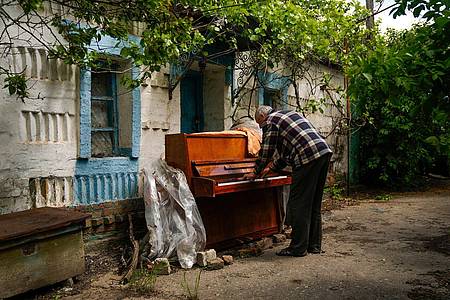 Anatolii Virko spielt Klavier vor einem Haus in Welyka Kostromka, das während der russischen Invasion beschädigt wurde.