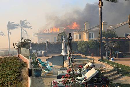 Flammen eines windgetriebenen Lauffeuers zerstören ein Gebäude in Kalifornien.