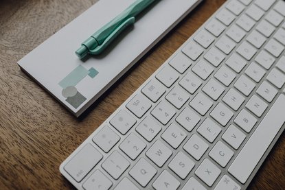 Tastatur, Block und Stift auf einem Holztisch.