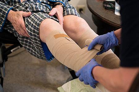 Eine ambulante Pflegerin bandagiert die Beine eines alten Mannes.