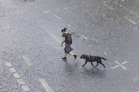 Eine Frau rennt mit ihrem Hund bei Starkregen in Köln über eine überflutete Straße.