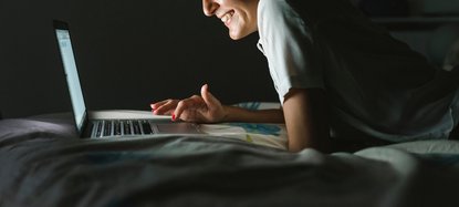 Frau liegt mit Laptop auf dem Bett