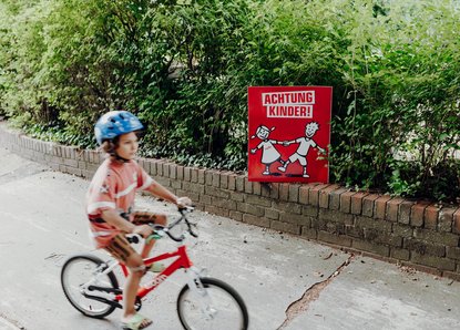 Spielendes Kind vor einem Achtung Kinder Plakat