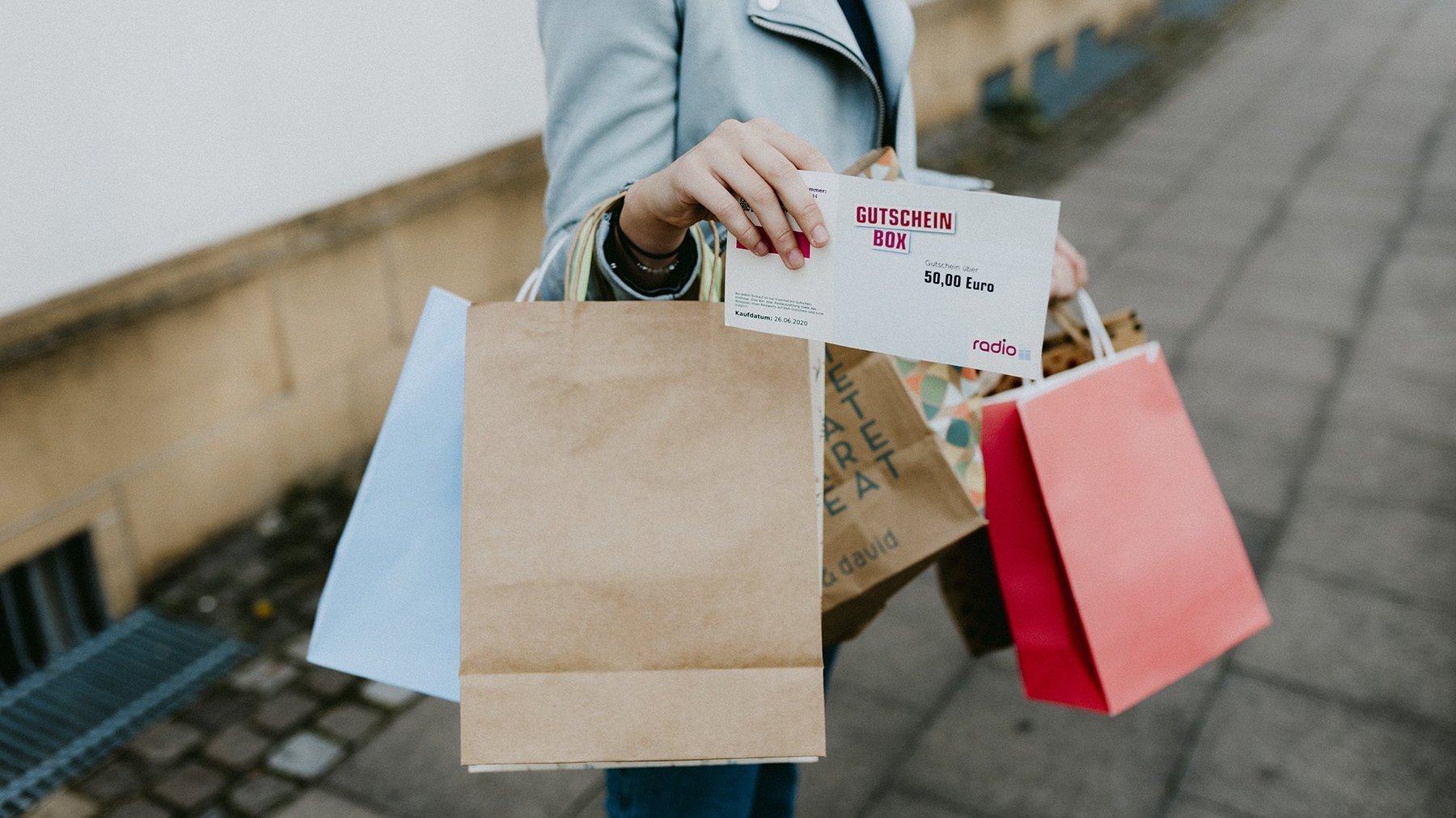 Frau hält viele Taschen in der Hand und einen Gutschein