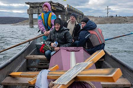 Eine Frau sitzt in einem Boot, das den Fluss Siverskyj-Donez überquert, um den Sarg ihres toten Sohnes zu transportieren, der bei Kämpfen mit den Russen gefallen ist.