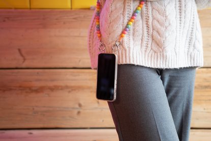 Frau hat Smartphone an bunter Handykette umgehängt.