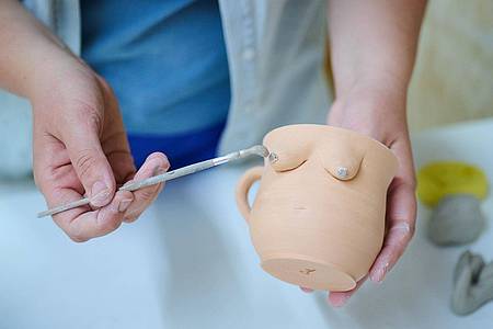 Catharina Rubel malt an einer getöpferten Tasse mit Brüsten die die Brustwarzen an.