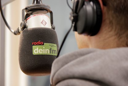 Person sitzt vor einem deinfm Mikrofon