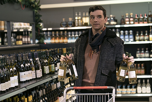 Peter befüllt seinen Einkaufswagen mit mehreren Flaschen Wein.