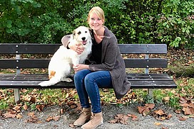 Mara sitzt mit einem Hund auf einer Bank