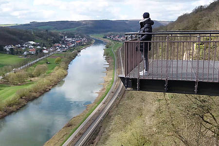 Eine Frau steht auf der Aussichtsplattform "Weser-SkyWalk" unter ihr erkennt man die Weser